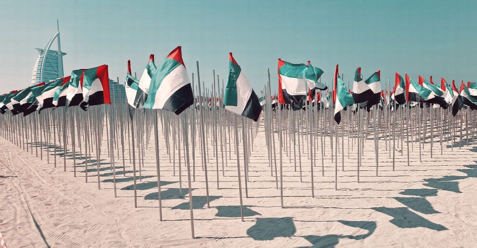 Rows of UAE flags on a sunny beach in Dubai, with Burj Al Arab in the background. Rows of UAE flags on a sunny beach in Dubai, with Burj Al Arab in the background.