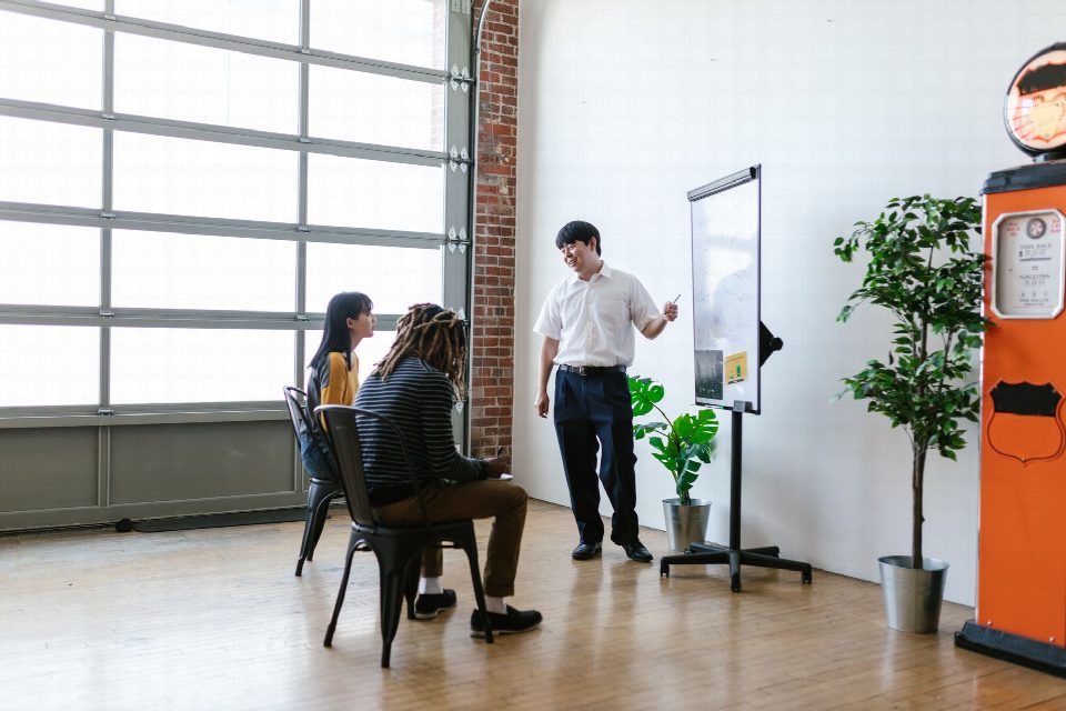 A meeting in a modern office with a presenter explaining concepts on a whiteboard. A meeting in a modern office with a presenter explaining concepts on a whiteboard.