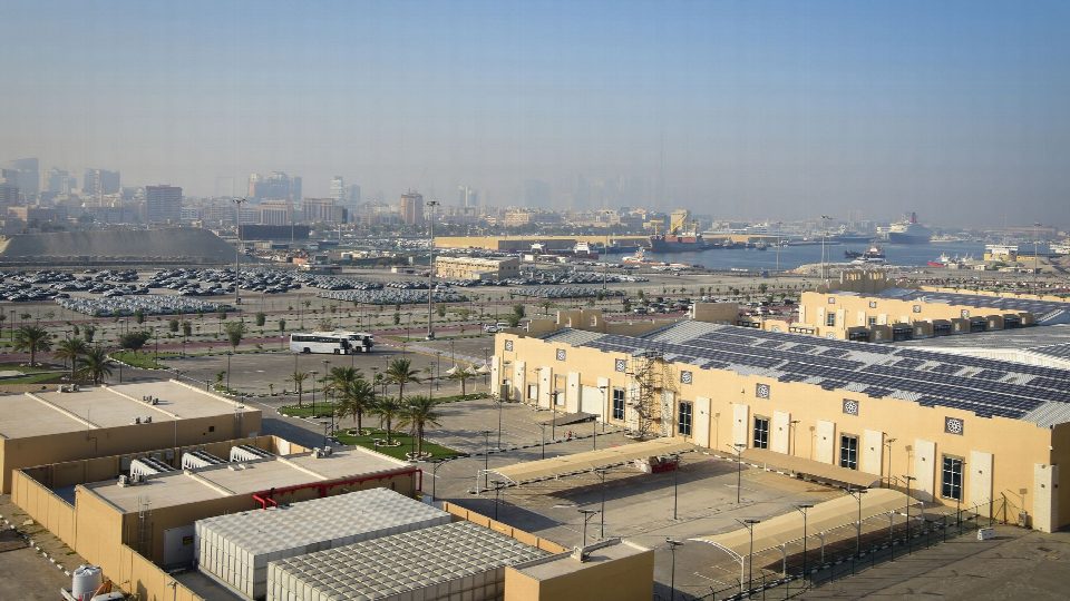 Aerial view of Dubai's harbor showcasing industrial buildings and distant skyline under a clear blue sky. Aerial view of Dubai's harbor showcasing industrial buildings and distant skyline under a clear blue sky.